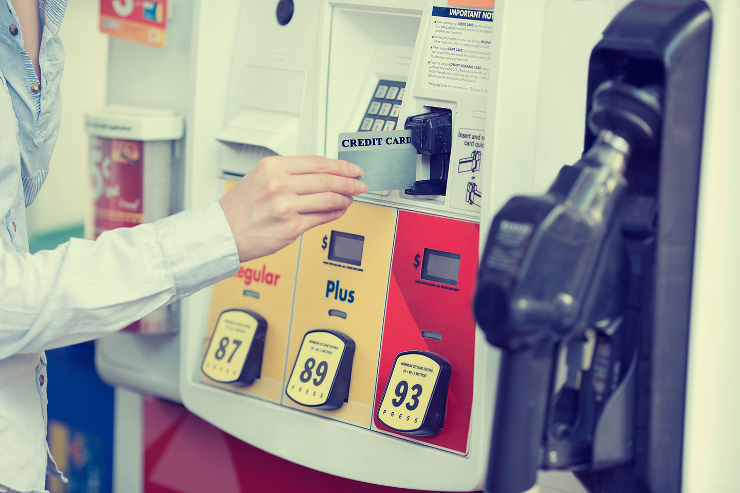 A woman inserts a credit card at the fuel pump at a a gas station.