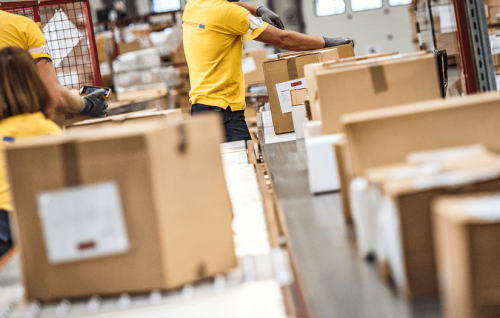 A shipping warehouse conveyer belt with packages are being sorted by workers in yellow shirts.