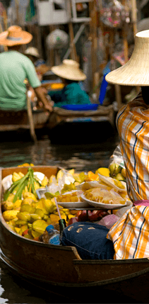A Thailand woman rows a canoe with exotic fruit inside.