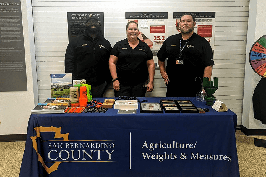 Three County Agriculture/Weights & Measures staff stand at a display table at the San Bernardino County Victor Valley Museum in Victorville for the Arthropolooza: The Ultimate Bugfest event in March 2024.