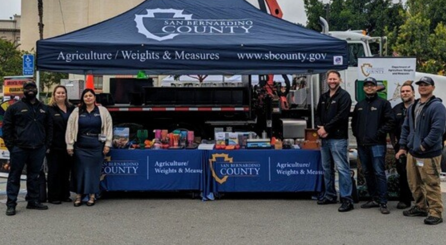 A group of Agriculture/Weights & Measures staff stand posed in front of a popup tent with the department name.